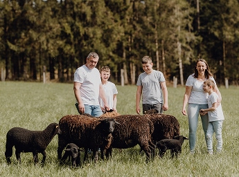 Die Eigentümer-Familie von Wollstixx steht umgeben von ihren Schafen auf einer Wiese.
